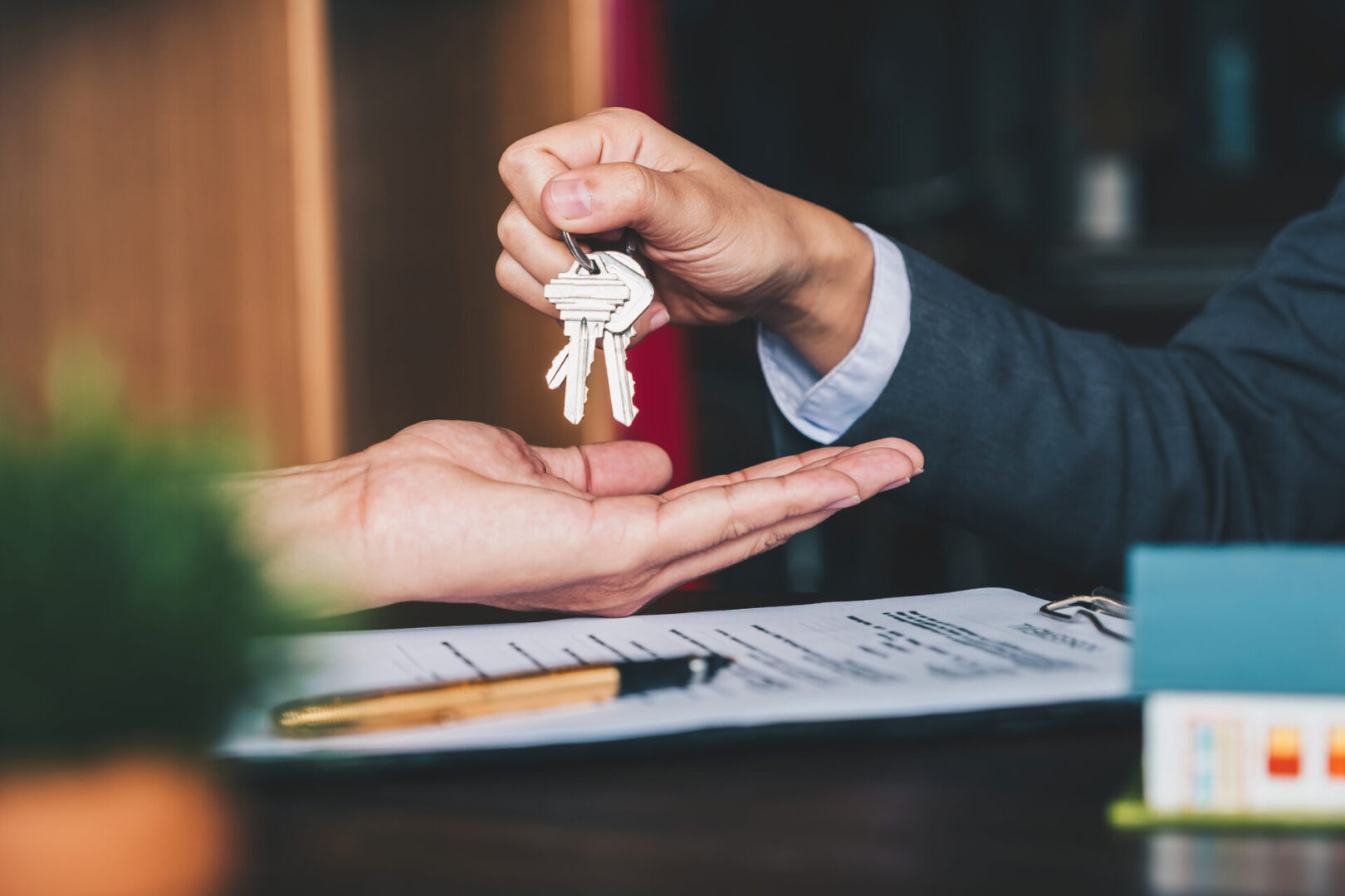 estate agent giving house keys to woman and sign agreement in office Handing over keys above contract and pen.